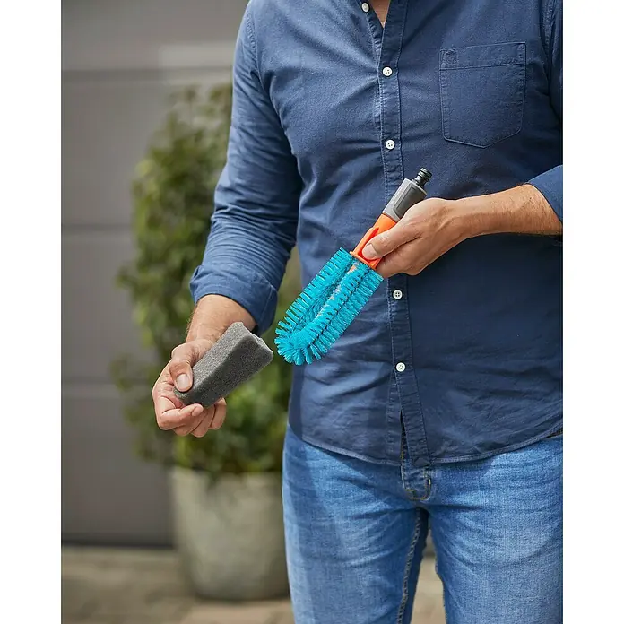 Gardena Reinigungsbürste Cleansystem - Wasserführend - Eine Person hält die GARDENA Waschbürste und einen Schwamm, ideal für die sanfte Reinigung von Fahrzeugen und Oberflächen im Außenbereich.