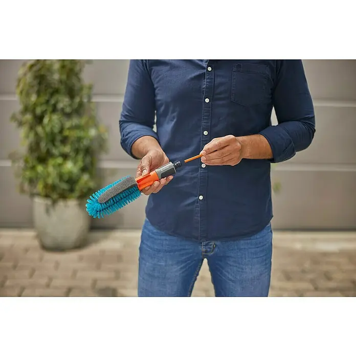 Gardena Reinigungsbürste Cleansystem - Wasserführend - Eine Person hält eine GARDENA Waschbürste mit Gelenk, die vielseitig für Reinigungsarbeiten im Außenbereich einsetzbar ist.