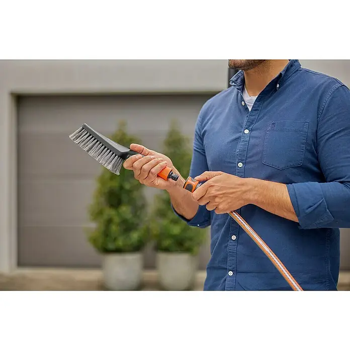 Gardena Waschbürsten-Set Cleansystem M Soft - Wasserführend - Nahaufnahme eines Mannes, der eine Bürste und einen Schlauchverbinder hält. Geeignet für die Reinigung von Oberflächen im Außenbereich.