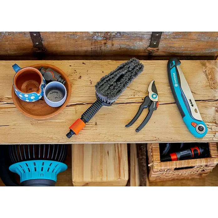 Gardena Waschbürsten-Set Cleansystem M Soft - Wasserführend - Gartengeräte auf einem Regal. Eine Bürste, eine Gartenschere und eine Säge der Marke Gardena sind zu sehen.