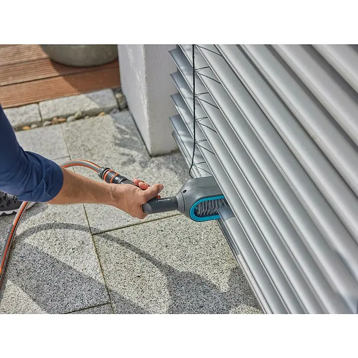 Gardena Reinigungsbürste Cleansystem - Passend für: Jalousien mit C- oder Z-Lamellen - Eine Person benutzt eine GARDENA Reinigungsbürste an Jalousien, angeschlossen an einem orangefarbenen Wasserschlauch.