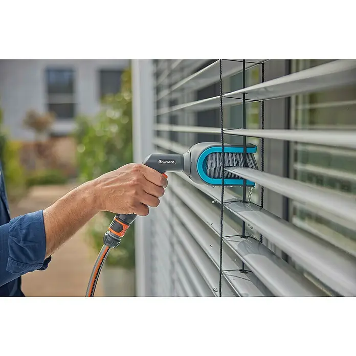 Gardena Reinigungsbürste Cleansystem - Passend für: Jalousien mit C- oder Z-Lamellen - Eine Person reinigt Jalousien mit einer Gardena Bürste, die an einen Schlauch angeschlossen ist. Praktische Gartenarbeit leicht gemacht.