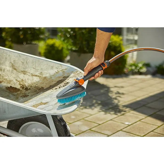 Gardena Cleansystem Handbürste Cleansystem M hard - Wasserführend - Eine Hand reinigt eine schmutzige Schubkarre mit einer Gardena Waschbürste und Wasserschlauch. Ideal für die Gartenarbeit.