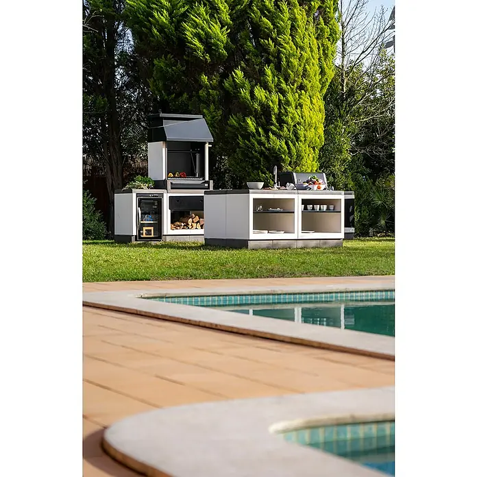 Tuozi Kitaway Holzkohlegrill - Grau/Weiß, B x T x H: 84 x 63 x 206 cm, Feinjustierung der Höhe durch Kurbel - Ein Blick auf eine stilvolle Outdoor-Küche mit Grill und Arbeitsflächen neben einem Pool, ideal für sommerliche Gartenpartys.