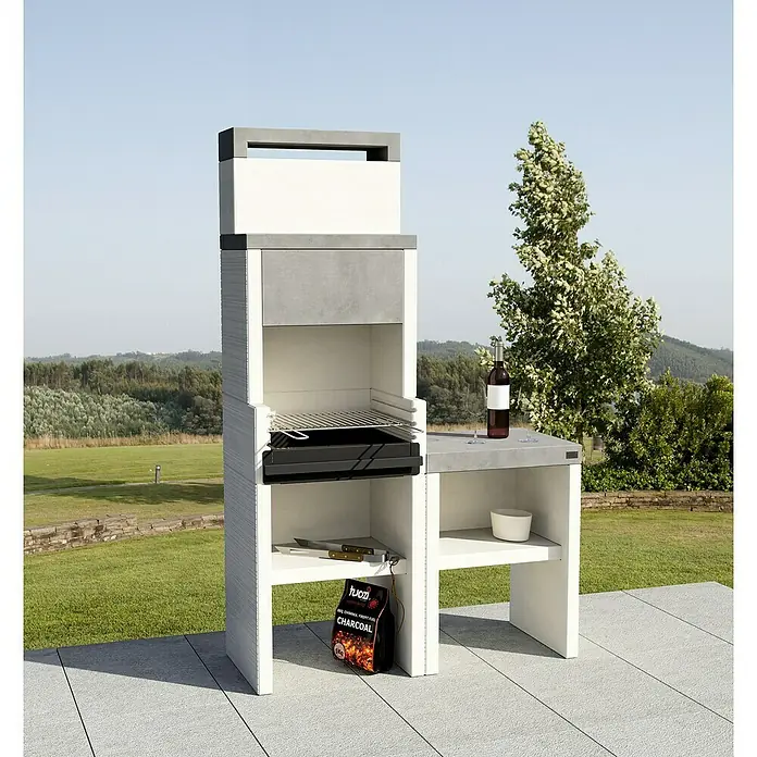 Tuozi Venit Outdoorküchen-Modul Seitenschrank - Weiß-Grau, B x T x H: 59 x 47 x 88 cm - Bild eines modernen Außengrills mit Betonarbeitsfläche, inklusive Holzkohlesack und Zubehör, auf einer Terrasse im Garten.