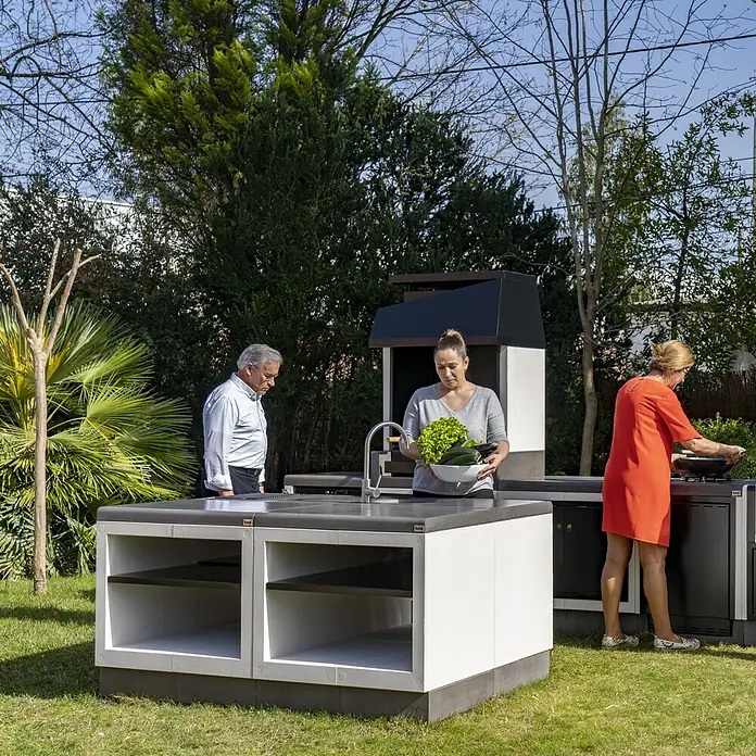 Tuozi Kitaway Outdoorküchen-Modul - Grau/Weiß, B x T x H: 84 x 63 x 85 cm - Gartenküche im Freien mit Spüle, Grill und Stauraum. Drei Personen bereiten Speisen zu.