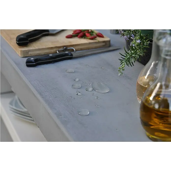 Tuozi Venit Outdoorküchen-Modul Seitenschrank - Weiß-Grau, B x T x H: 78 x 47 x 88 cm - Nahaufnahme einer Küchenarbeitsplatte mit Messern, Schneidebrett, Chilischoten und Ölkaraffen, die eine saubere und kulinarische Ästhetik erzeugt.