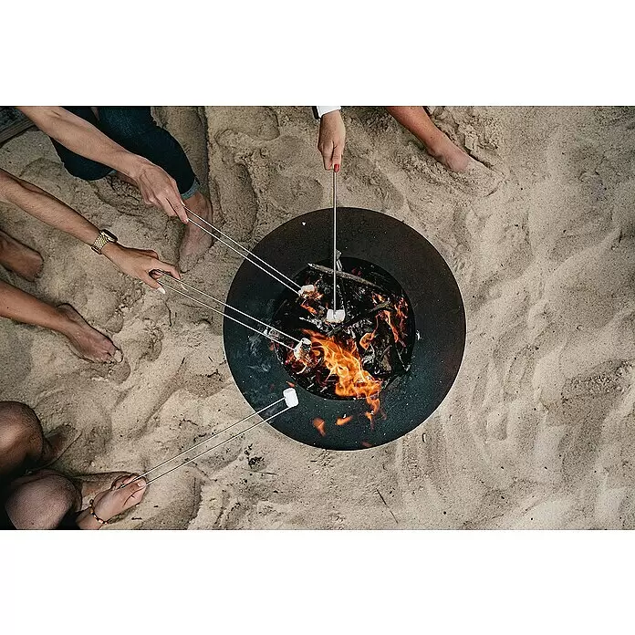 Tuozi Feuerschale Phobos - L x B x H: 60 x 60 x 24 cm, Cortenstahl - Schwarze, runde Feuerschale mit Marshmallows über Flammen am Sandstrand.