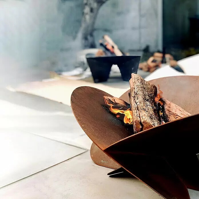 Tuozi Feuerschale Medusae - L x B x H: 75 x 75 x 35 cm, Cortenstahl - Rostfarbene Metall-Feuerschale für den Außenbereich mit brennenden Holzscheiten auf einer Terrasse.