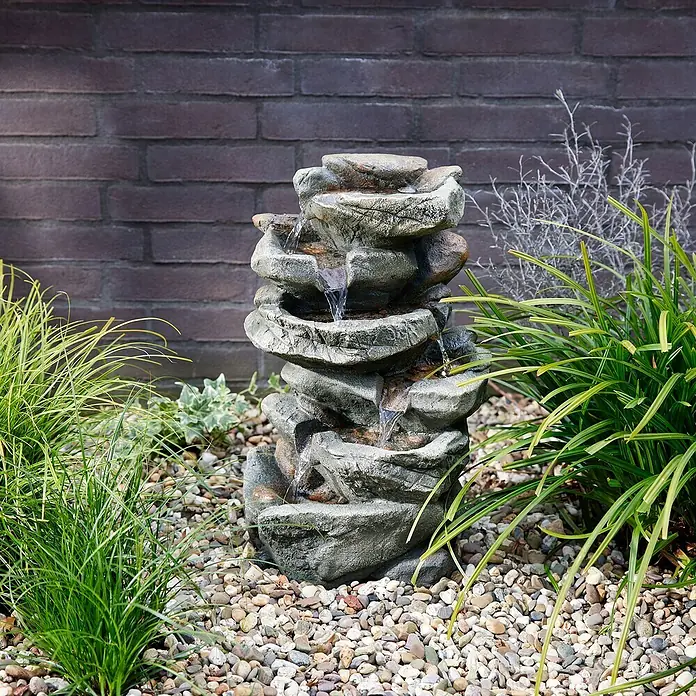 Fuente de jardín Caselle - 26 x 36 x 50 cm - Primer plano de una pintoresca fuente de roca con múltiples cascadas, rodeada de exuberante vegetación y piedras decorativas.