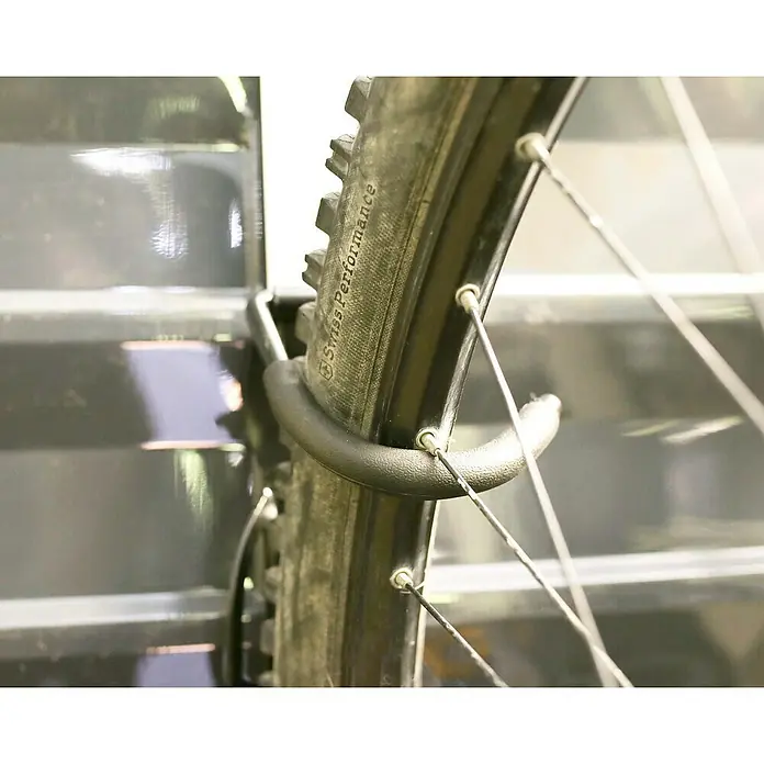 Palram – Canopia Fahrrad-Wandhaken - Passend für: Mountainbikes mit Laufrädern von 36 bis 74 cm (14" bis 29") - Nahaufnahme eines Fahrradreifens auf einer Fahrradaufbewahrung, der mit einem Reifenhalter sicher an seinem Platz gehalten wird.