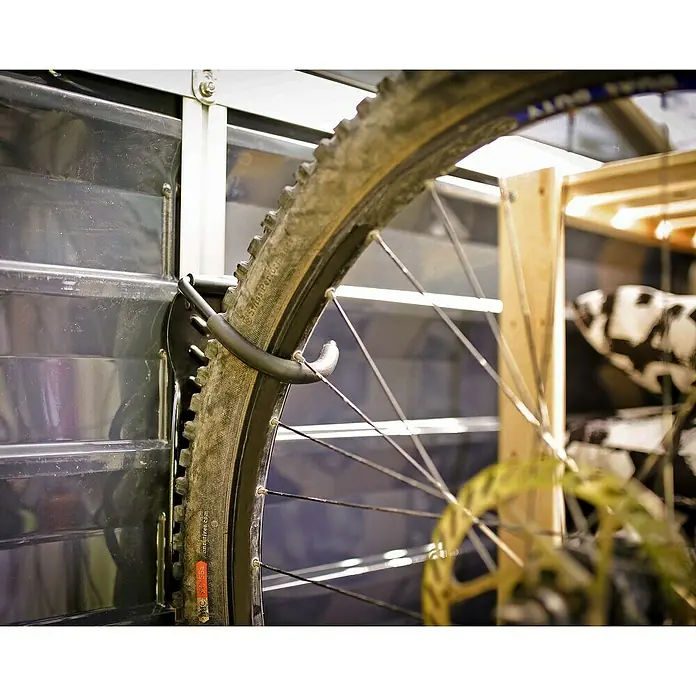 Palram – Canopia Gancho de pared para bicicletas - 3 ud., Específico para: Bicicletas de montaña con ruedas de 36 a 74 cm (14" a 29") - Detalle de un neumático de bicicleta montado en un soporte de pared, centrándose en la banda de rodadura y los radios.