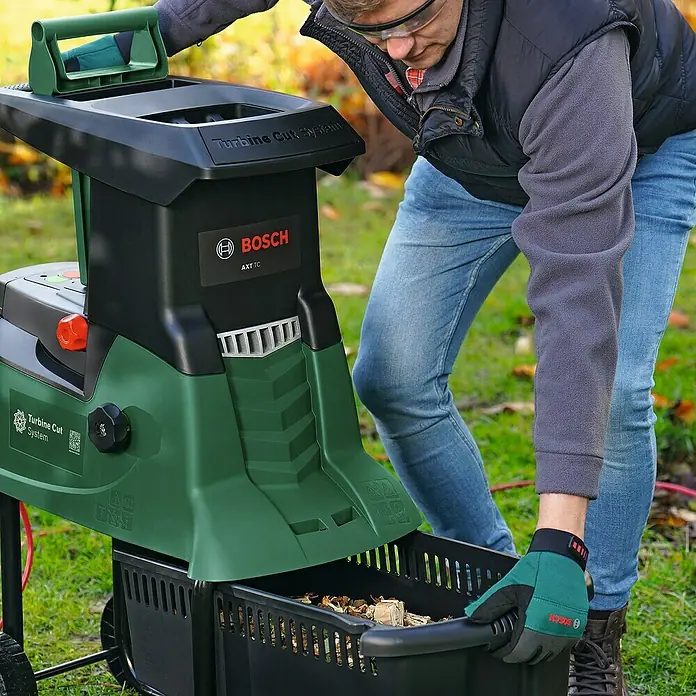 Bosch Elektro-Häcksler AXT 25 TC - Max. Aststärke: 4,5 cm, 2.500 W - Ein Mann leert einen Bosch AXT TC Gartenhäcksler in einen Behälter, um Gartenabfälle zu zerkleinern.
