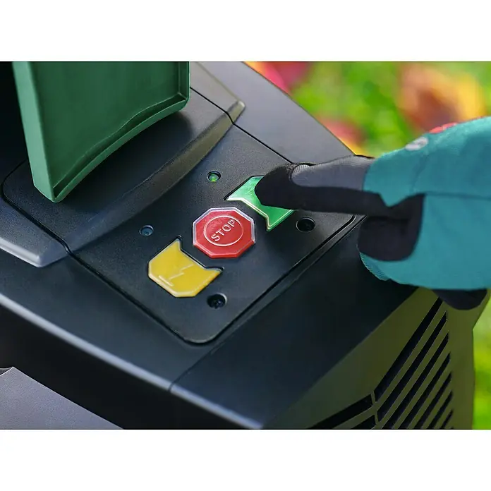 Bosch Elektro-Häcksler AXT 25 TC - Max. Aststärke: 4,5 cm, 2.500 W - Nahaufnahme einer Person, die mit einem Handschuh einen grünen Startknopf an einer elektrischen Maschine bedient.