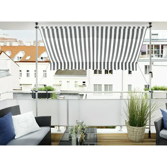 Sunfun Klemmmarkise - Grau/Weiß, Breite: 3 m, Ausfall: 1,3 m - Eine gestreifte Markise überdacht eine Terrasse mit Rattanmöbeln, einem Glastisch und üppigem Grün. Die Markise bietet Schatten und Privatsphäre.