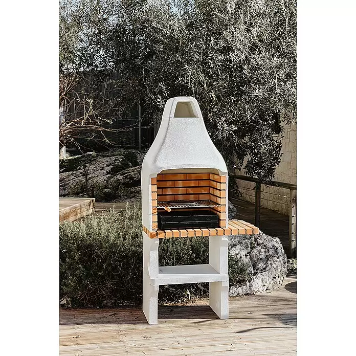 Movelar New Iberia Holzkohlegrill - Grillfläche (B x T): 56 x 35 cm, Grau, B x T x H: 95 x 47 x 190 cm - Weißer Beton-Außengrill mit Ziegelauskleidung und Holznebentisch auf Holzterrasse im Garten.