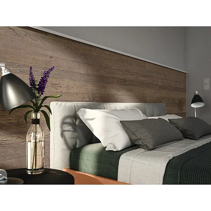 Egger Wandpaneel DecoWall - Annaba Eiche Natur, 125 cm x 66 cm x 12 mm - Nahaufnahme eines Bettes mit grauen Kissen, einer Holzwand und einem modernen Lampendesign für eine gemütliche Schlafzimmeratmosphäre.