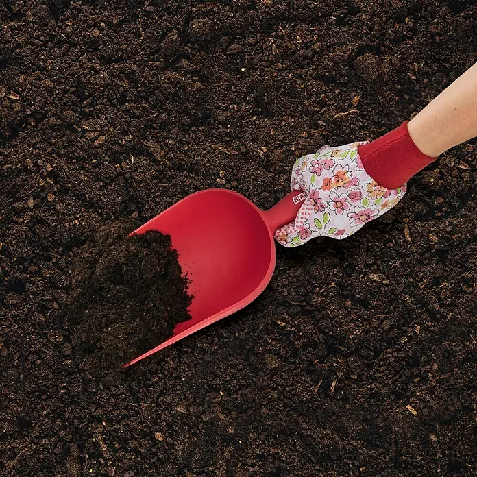 BAUHAUS Schaufel XXL - 12 cm, Rot - Nahaufnahme eines roten Pflanzspatens, der in Erde gehalten wird, ideal für Gartenarbeiten und kleine Pflanzprojekte.
