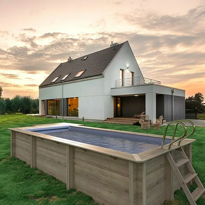 myPool Holz-Pool Urban - 670 x 301 x 133 cm, 11.800 l, Braun, Grau - Bild eines Holzpools im Garten eines modernen Hauses. Der Pool ist mit einer Leiter ausgestattet und lädt zum Entspannen ein.