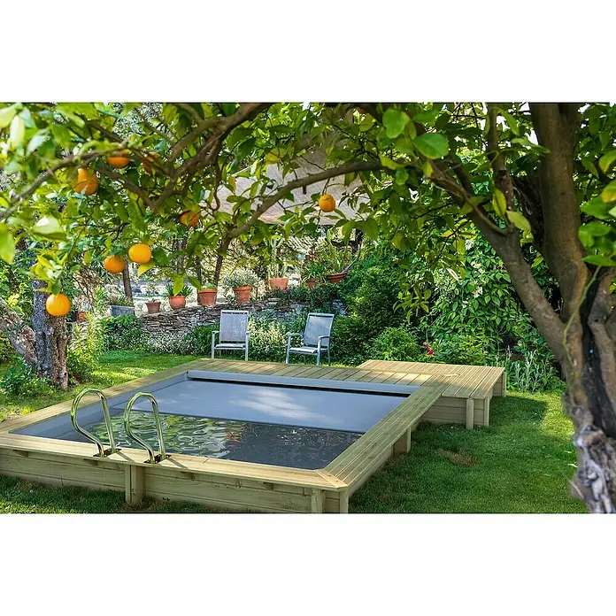 myPool Holz-Pool Urban - 486 x 401 x 133 cm, 11.000 l, Braun, Grau - Gartenszene mit einem kleinen hölzernen Pool mit silberner Leiter und Abdeckung, umgeben von Bäumen, Pflanzen und Gartenmöbeln.