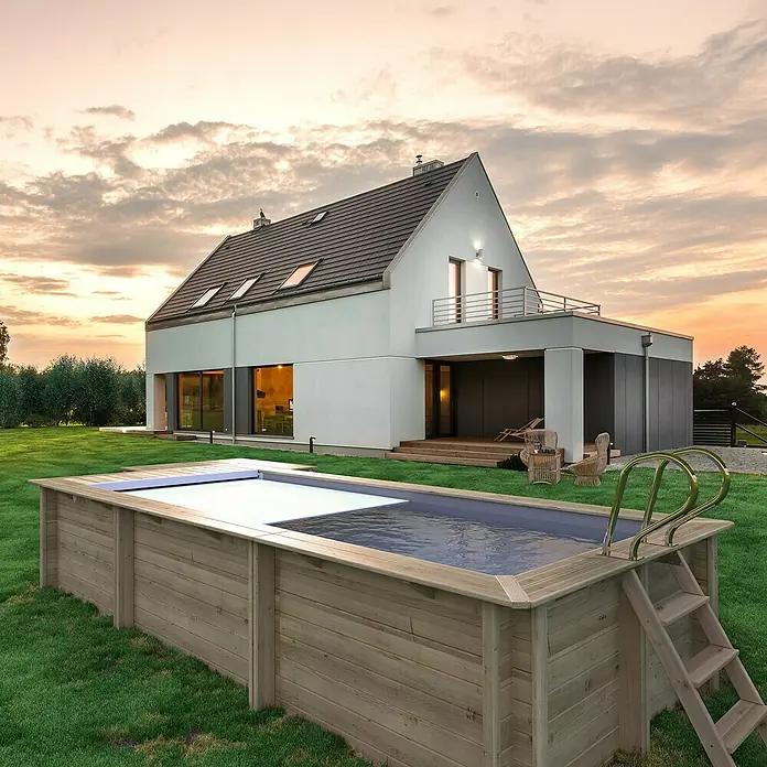 myPool Holz-Pool Urban - 670 x 301 x 133 cm, 11.800 l, Braun, Grau - Holzpool mit Leiter und teilweise geöffneter Abdeckung im Garten eines modernen Hauses bei Sonnenuntergang.