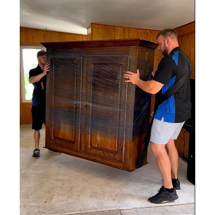 Tragegurt - Traglast: 370 kg - Zwei Umzugshelfer tragen einen großen, mit Folie verpackten Holzschrank. Die Helfer sind mit Tragegurten ausgestattet.
