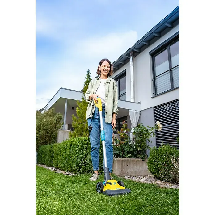 Gloria Elektro-Rasenmäher FineCut 230V - 60 W, Schnittbreite: 25 cm - Frau benutzt einen gelben Rasenkantenschneider auf einem Rasen vor einem Haus.