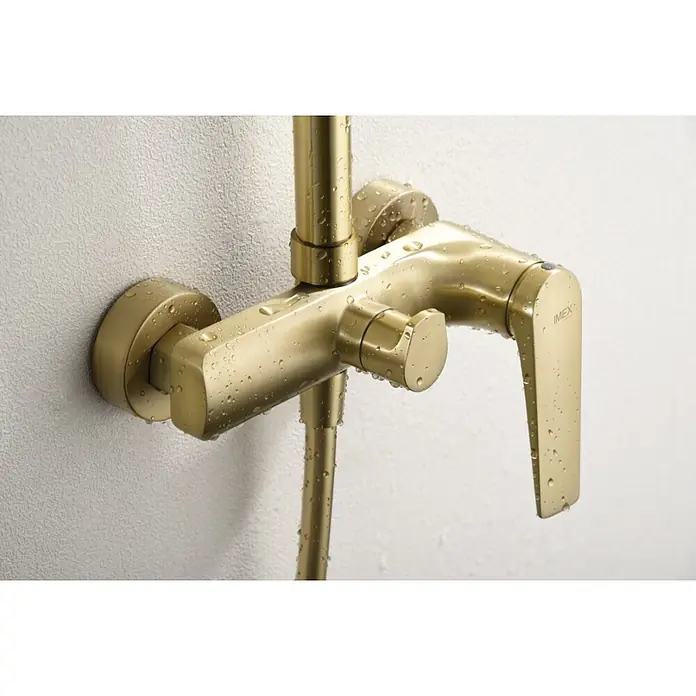Imex Delos Sistema de ducha - Grifo monomando, Oro - Primer plano de un mezclador de ducha IMEX de color dorado con gotas de agua sobre una pared blanca texturizada.