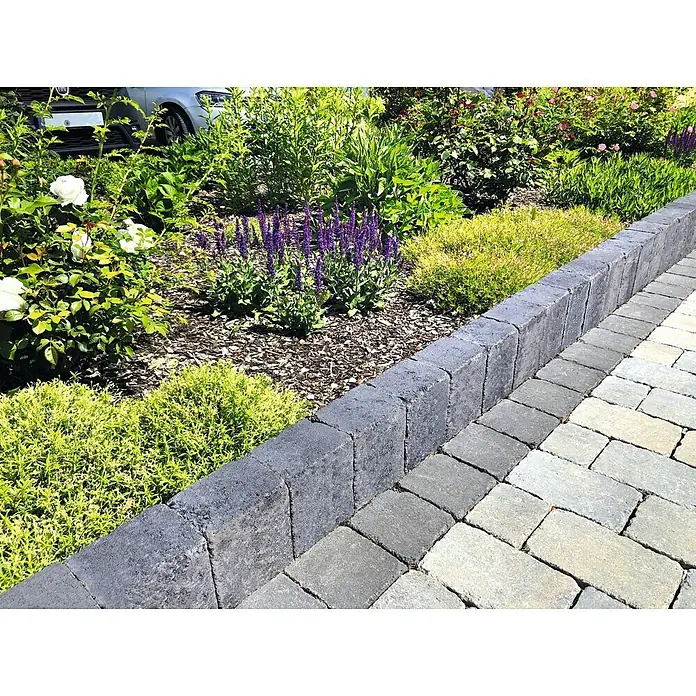Christoph Mauerstein Collo-Block - 60 x 10,5 x 14 cm, Anthrazit, Beton - Nahaufnahme eines Zierpflasters mit grauen Pflastersteinen und einer Bordsteinkante, die einen gepflegten Garten von einem Weg trennt.