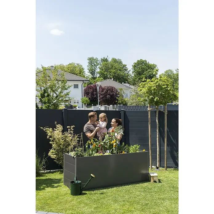 Guardi Hochbeet - 140 x 70 x 76 cm, Metall, Anthrazit - Familie steht an einem erhöhten, grauen Gartenbeet mit frischem Gemüse, einem grünen Rasen und einer grünen Gießkanne im Vordergrund.