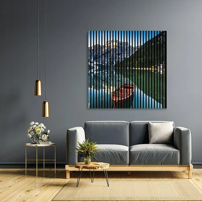 Profiles and more Akustikpaneel Dolomiten - 1.195 x 1.133 x 19 mm - Ein Wohnzimmer mit einem grauen Sofa und einem Wandbild von einem Bergsee mit Boot, das dem Raum eine ruhige Atmosphäre verleiht.