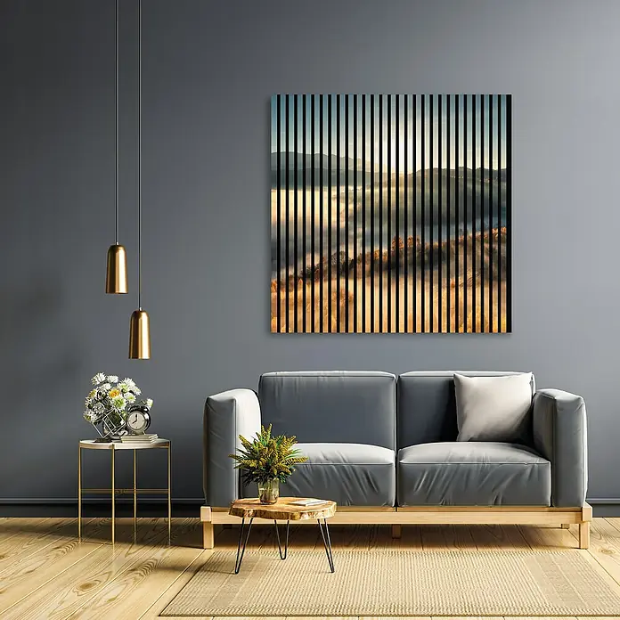 Profiles and more Akustikpaneel Sunrise - 1.195 x 1.133 x 19 mm - Ein Wohnzimmer mit grauem Sofa, goldenen Lampen und einem abstraktem Wandbild mit vertikalen Streifen und Landschaftsmotiv.