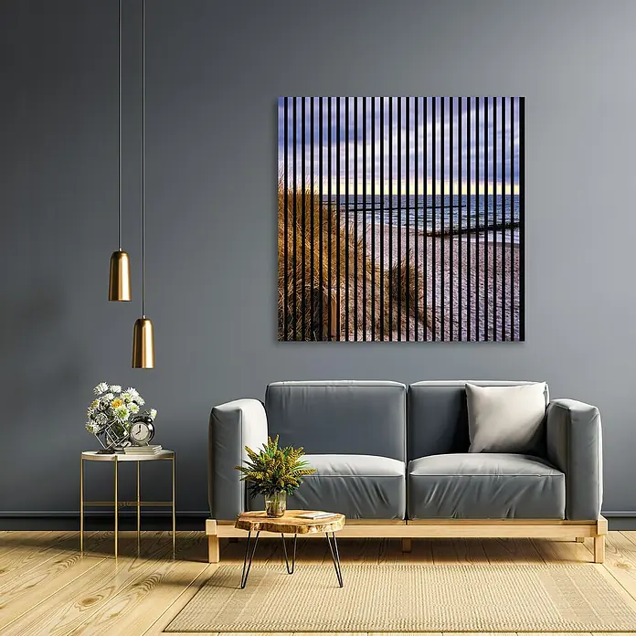 Profiles and more Akustikpaneel Ostsee - 1.195 x 1.133 x 19 mm - Ein Wohnzimmer mit einem grauen Sofa, einem Beistelltisch mit Blumen und einer abstrakten Strandkunst, die die Atmosphäre des Raumes betont.