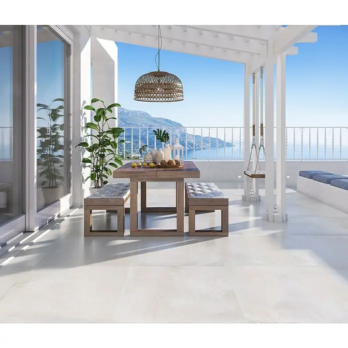 Feinsteinzeugfliese Chateau - 100 x 100 cm, Weiß/Beige, Matt - Elegante Terrasse mit Holztisch und Bänken unter einer dekorativen Hängelampe, ideal für Mahlzeiten im Freien mit Meerblick.