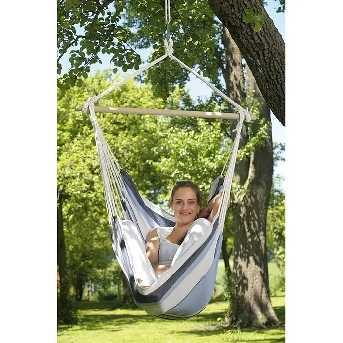 Amazonas Hängesessel Havanna marine - L x B x H: 150 x 120 x 110 cm, Blau/Weiß - Frau entspannt in einem gestreiften Hängehängesessel mit Holzspreizstab im Garten, der an einem Baum befestigt ist.