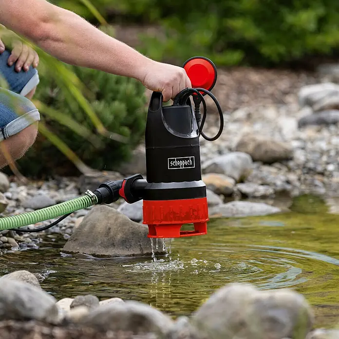 Scheppach Schmutzwasserpumpe DWP750 - Max. Fördermenge: 20.000 l/h - Der Scheppach Tauchpumpe, ein zuverlässiges Gerät zum Abpumpen von Wasser, wird über einen Teich gehalten, um Wasser abzupumpen.