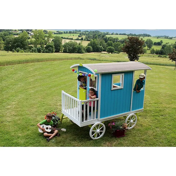 Soulet Spielhaus Carry - L x B x H: 262 x 155 x 203 cm, Holz - Kinder spielen in einem blauen Spielwagen auf Rädern mit weißem Geländer und Dekorationen. Ein Kind spielt Gitarre davor.
