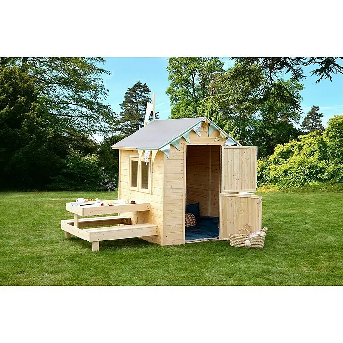 Soulet Spielhaus Blanche - L x B x H: 302 x 127 x 162 cm, Holz - Ein hölzernes Spielhaus mit Picknicktisch und blaugrüner Wimpelkette auf einer grünen Wiese, umgeben von Bäumen, lädt zum Spielen im Freien ein.