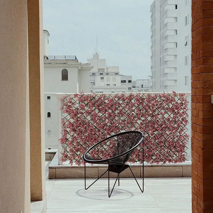 Celosía extensible Mimbre - An x Al: 2 x 1 m, Malva - Moderna silla de cesto negra en una terraza con vistas a la ciudad, rodeada de paredes de flores decorativas.
