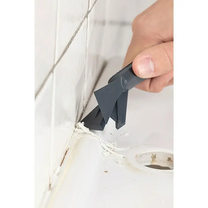 Wolfcraft Rascador de juntas - 4 pzs. - Primer plano de una herramienta de remoción de lechada en acción, que elimina el sellador viejo entre las baldosas y un fregadero. Ideal para la renovación del baño o la cocina.