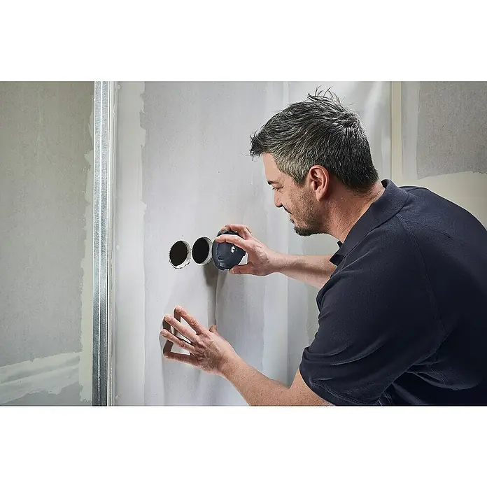Wolfcraft Kit de accesorios - 3 pzs., Específico para: Cajas de enchufes en pared hueca - Hombre inspeccionando recortes redondos en paneles de yeso con una herramienta. Presumiblemente, la herramienta sirve para el control de calidad.