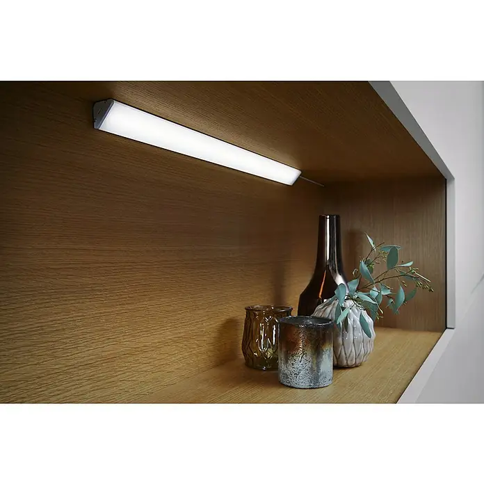 Ledvance Lámpara fluorescente LED Cabinet Corner - L x An x Al: 55 x 4,07 x 2,3 cm, Color de luz: Blanco cálido, 2 ud. - La imagen muestra una moderna luz LED bajo el gabinete que ilumina objetos decorativos en un estante de madera, proporcionando una iluminación elegante.