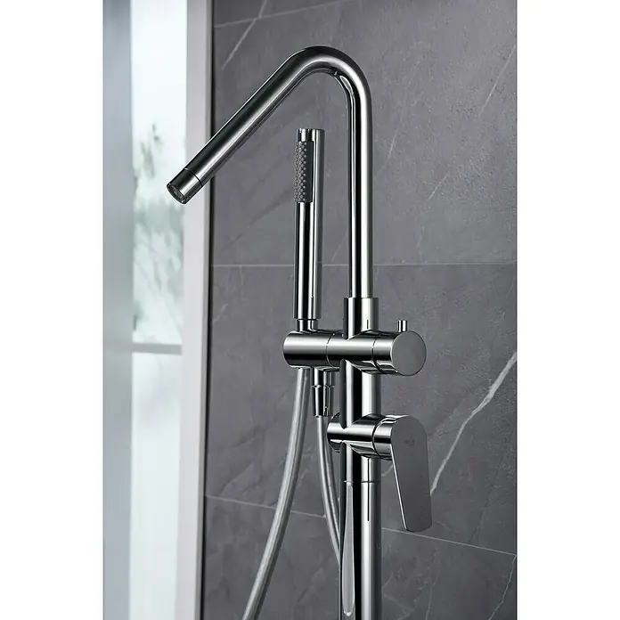 Imex Bélgica Grifo para bañera - Altura: 118 cm, Cromo, Brillante - Primer plano de un elegante grifo de bañera independiente cromado con teleducha y diseño moderno sobre una pared gris.