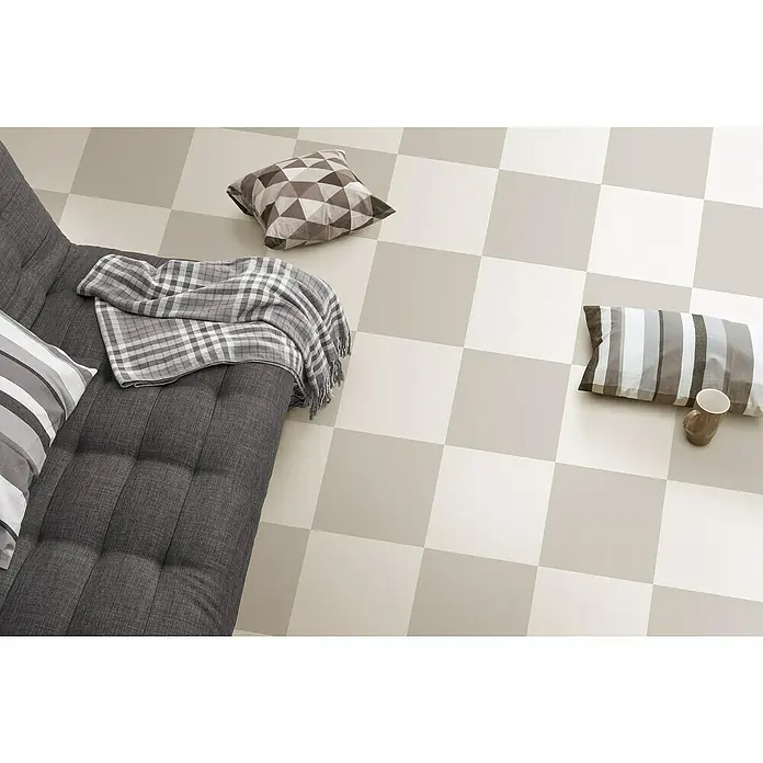 Feinsteinzeugfliese Barcelona Piedra - 24,8 x 24,8 cm, Beige, Matt - Ein graues Sofa mit Kissen und einer Decke auf einem Schachbrettboden. Das Design des Bodenbelags ist eine stilvolle Ergänzung für jeden Raum.