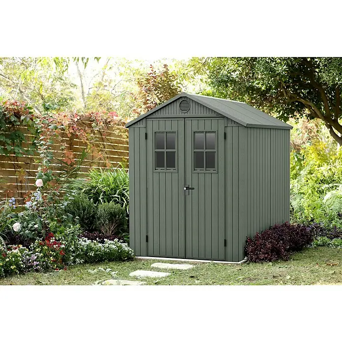 Keter Gartenhaus Darwin 6x6 - Außenmaß inkl. Dachüberstand (B x T): 190 x 183 cm, Kunststoff, Grün, 3,477 m² - Ein graues Gartenhaus mit Doppeltür und Fenstern steht in einem üppigen Garten, umgeben von Blumen und Grün. Ideal für Gartengeräte.