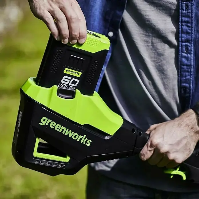 Greenworks 60V Akkusystem Cortasetos telescópico GD60PHT51 - 60 V, Iones de litio, Sin batería, Longitud de corte: 51 cm - Una persona inserta una batería Greenworks de 60 voltios en un cortabordes Greenworks alimentado por batería.