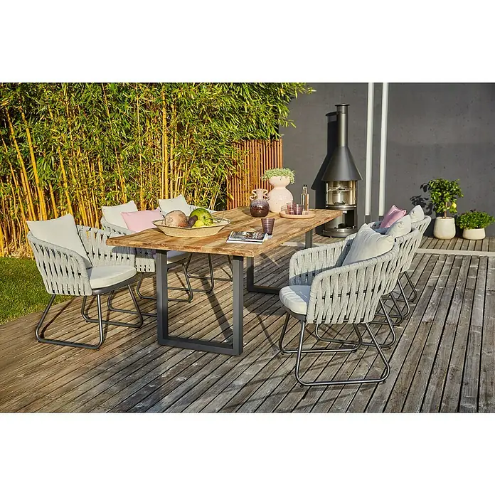 Sunfun Gartentisch - L x B x H: 220 x 100 x 75 cm, Edelstahl, Teak, Natur/Anthrazit, Baumkante/U-Fuß - Einladende Gartenszene mit einem Esstisch aus Holz und stilvollen grauen Stühlen auf einer Holzterrasse. Dekorative Elemente vervollständigen das Ambiente.