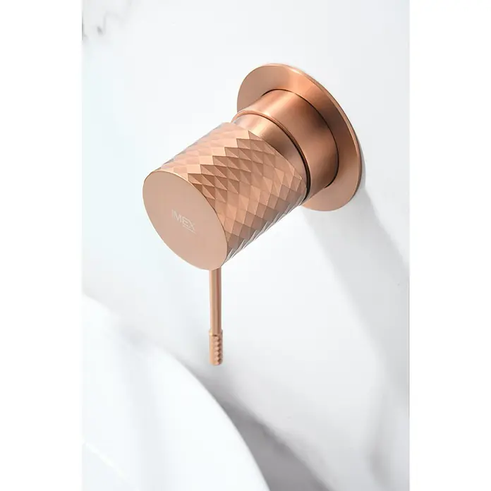 Imex Génova Grifo de lavabo empotrado - Oro rosa - Primer plano de un moderno grifo IMEX de oro rosa con patrón de diamante, montado en una pared blanca. Diseño de baño elegante.