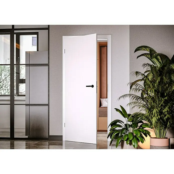 Invado Zimmertür ND1 ohne Schlüssellochbohrung860 x 1.985 mm, DIN Anschlag: Links, Verkehrsweiß matt, Röhrenspan - Die elegante weiße Tür mit schwarzem Griff öffnet sich zu einem stilvollen Raum, umgeben von modernem Design und Pflanzen.