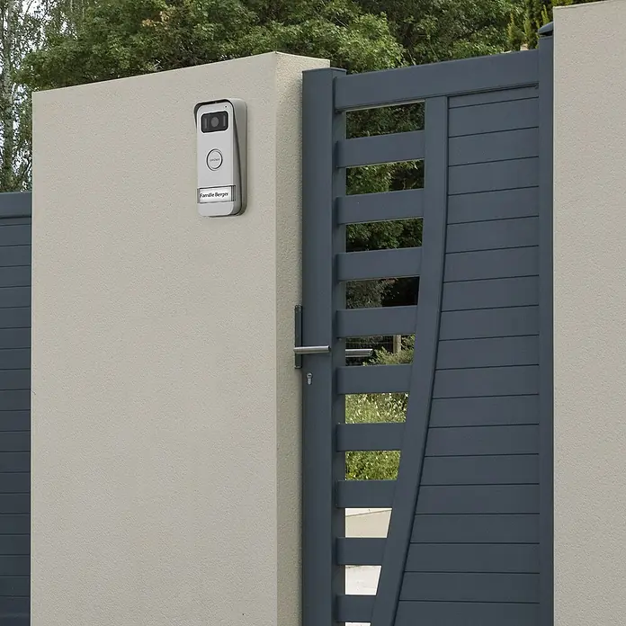 Avidsen Türklingel mit Kamera Smarte Video Türsprechanlage Elia - Weiß, Silber, 800 x 480 Pixel - Nahaufnahme einer modernen grauen Toranlage mit elektronischer Gegensprechanlage an einer beigen Säule, die Sicherheit und Stil vereint.